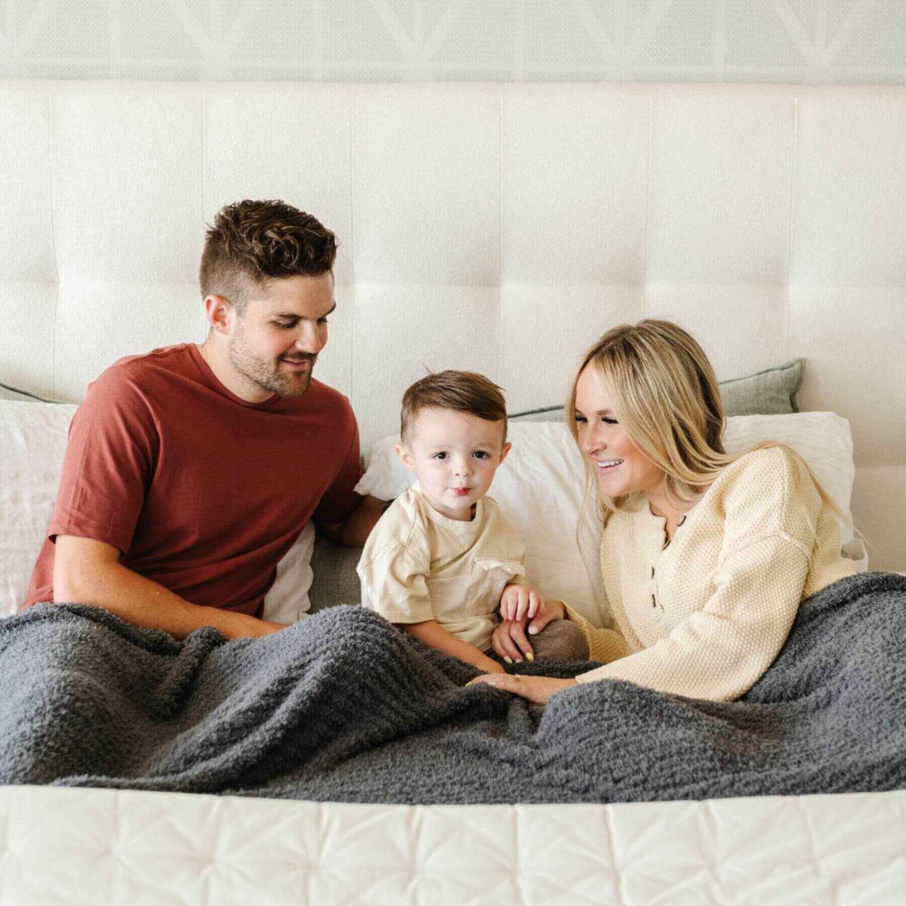Family of three sitting on a bed with aRibbed Bamboni® Throw Blanket Charcoal
