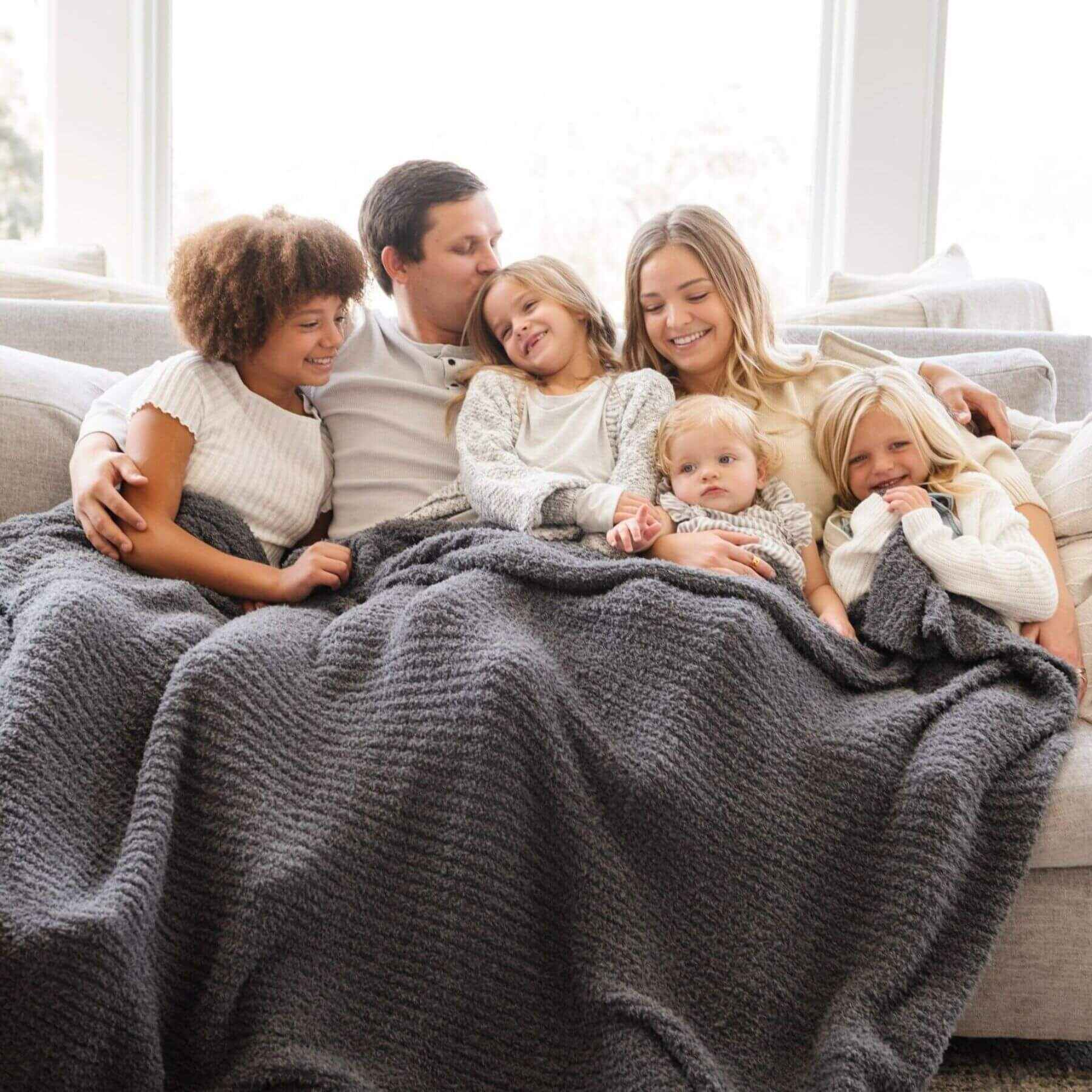 Family of five snuggling under Saranoni Ribbed Bamboni® XL Blanket - Charcoal on a couch in a bright room.