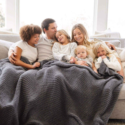 Family of five snuggling under Saranoni Ribbed Bamboni® XL Blanket - Charcoal on a couch in a bright room.