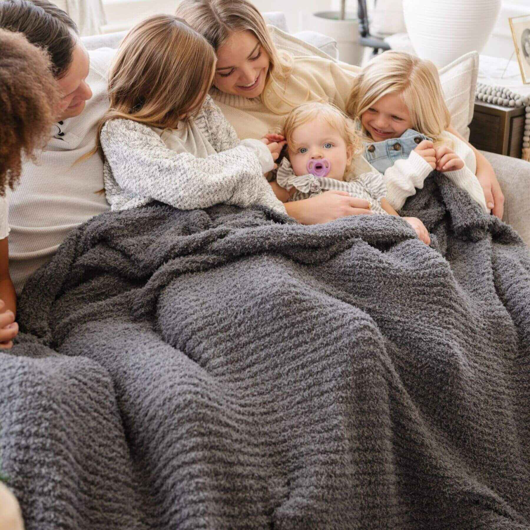 Family of five snuggling under Saranoni Ribbed Bamboni® XL Blanket - Charcoal in a cozy living room.