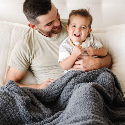 Man holding a child wrapped in Saranoni Ribbed Bamboni® XL Blanket - Charcoal on a white couch