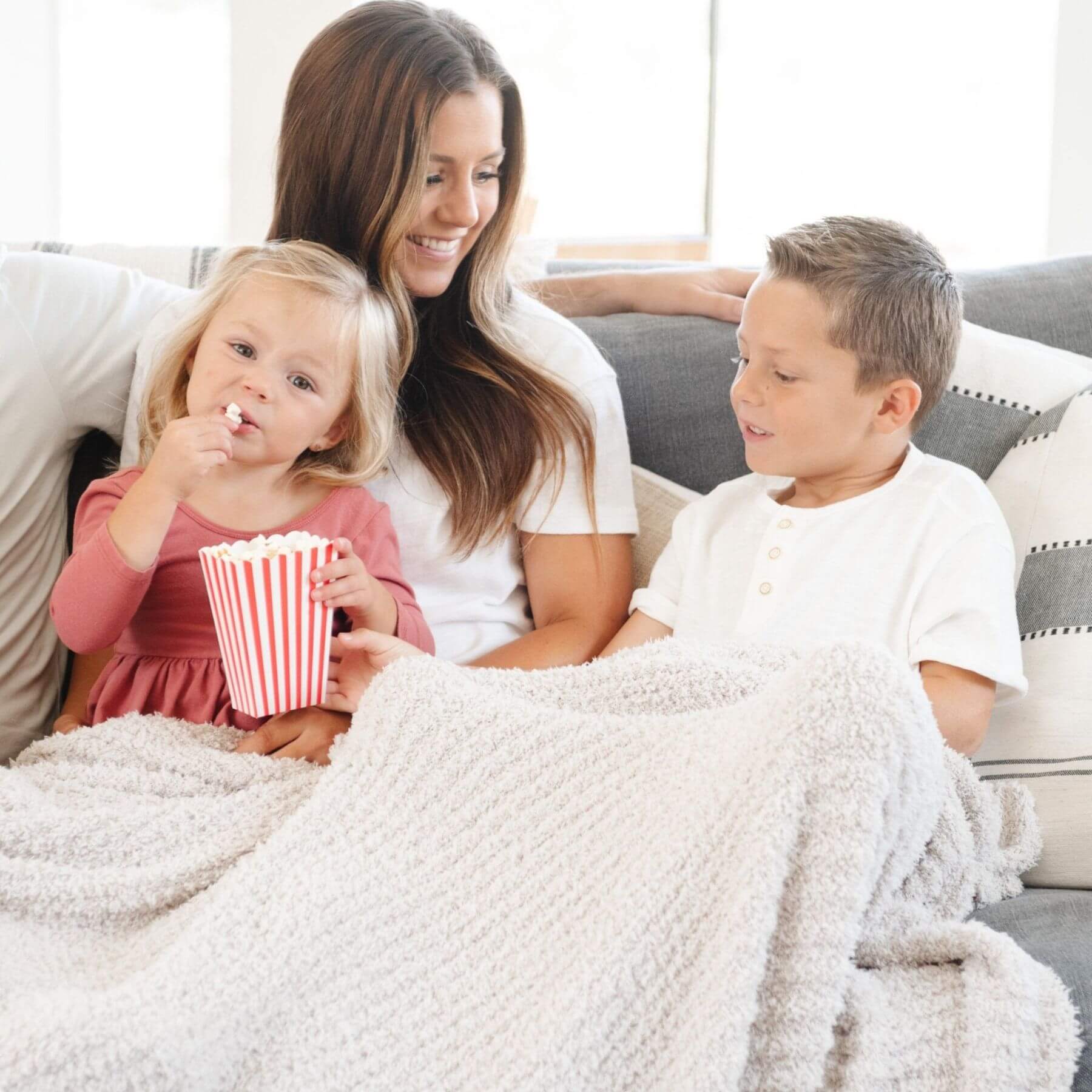 Woman and two children sitting on a couch with popcorn, wrapped in Saranoni Ribbed Bamboni® XL Blanket - Moonbeam