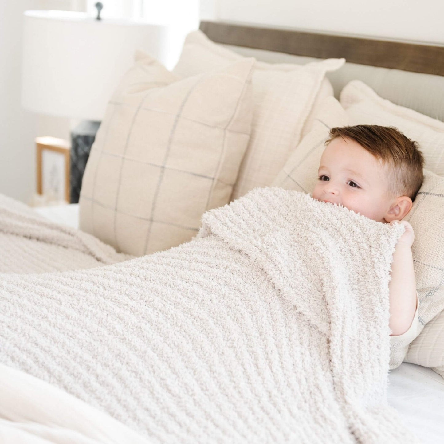 Baby wrapped in Saranoni Ribbed Bamboni® XL Blanket - Moonbeam on a bed with neutral tones