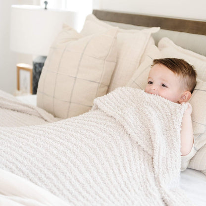 Baby wrapped in Saranoni Ribbed Bamboni® XL Blanket - Moonbeam on a bed with neutral tones