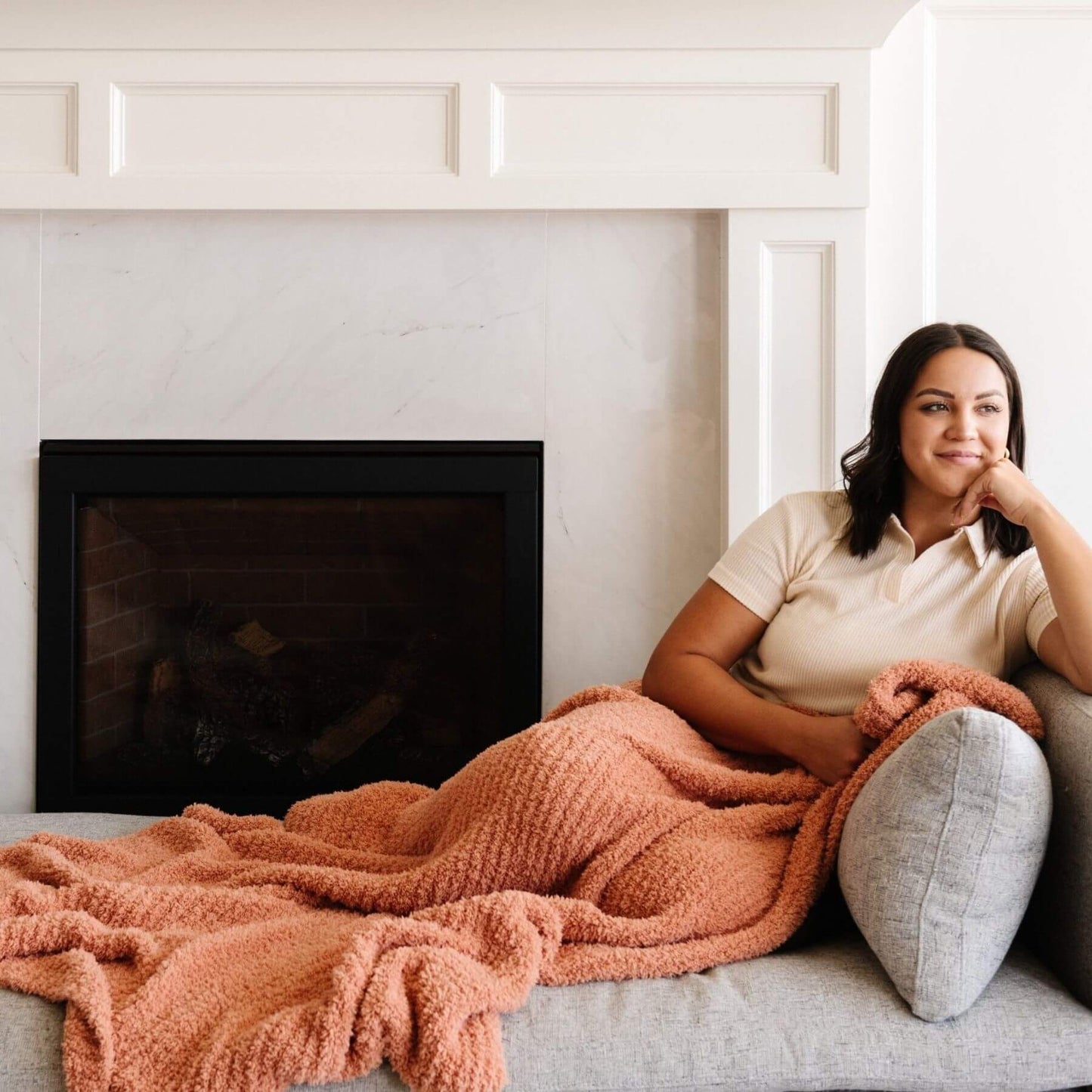 Woman sitting on a couch with Saranoni Ribbed Bamboni® XL Blanket - Sun-Kissed in front of a fireplace