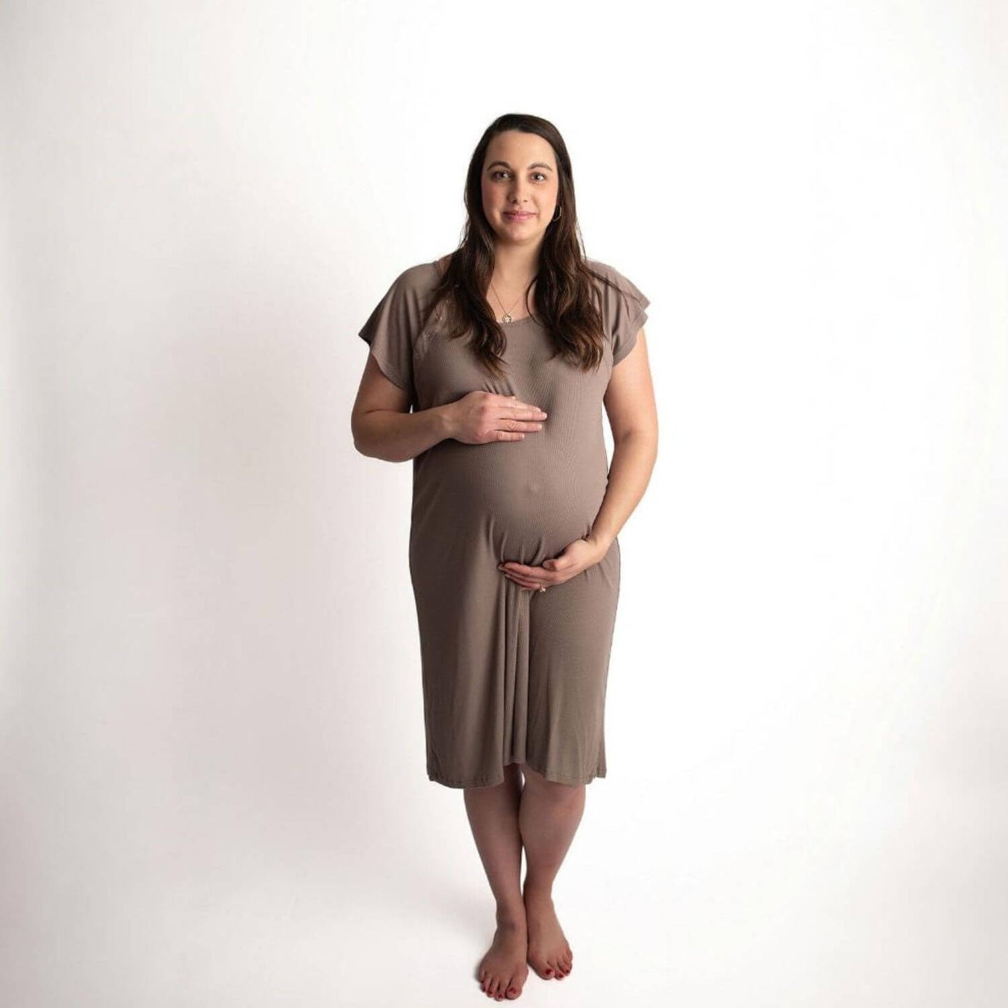 A pregnant woman stands barefoot against a plain white studio background, wearing Three Little Tots Ribbed Cocoa Brown Mommy Gown