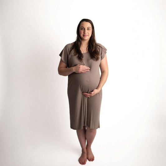 A pregnant woman stands barefoot against a plain white studio background, wearing Three Little Tots Ribbed Cocoa Brown Mommy Gown
