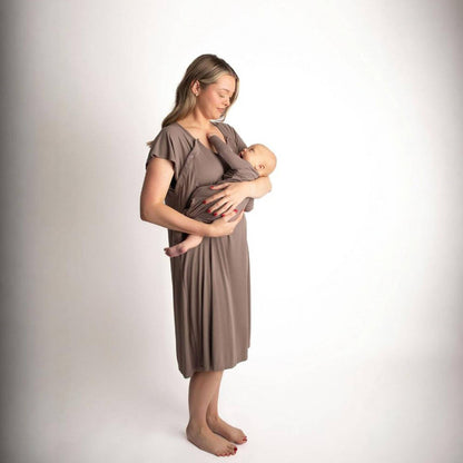 A woman wearing Three Little Tots Ribbed Cocoa Brown Mommy Gown holds a sleeping baby against her chest in a studio setting with a white background.