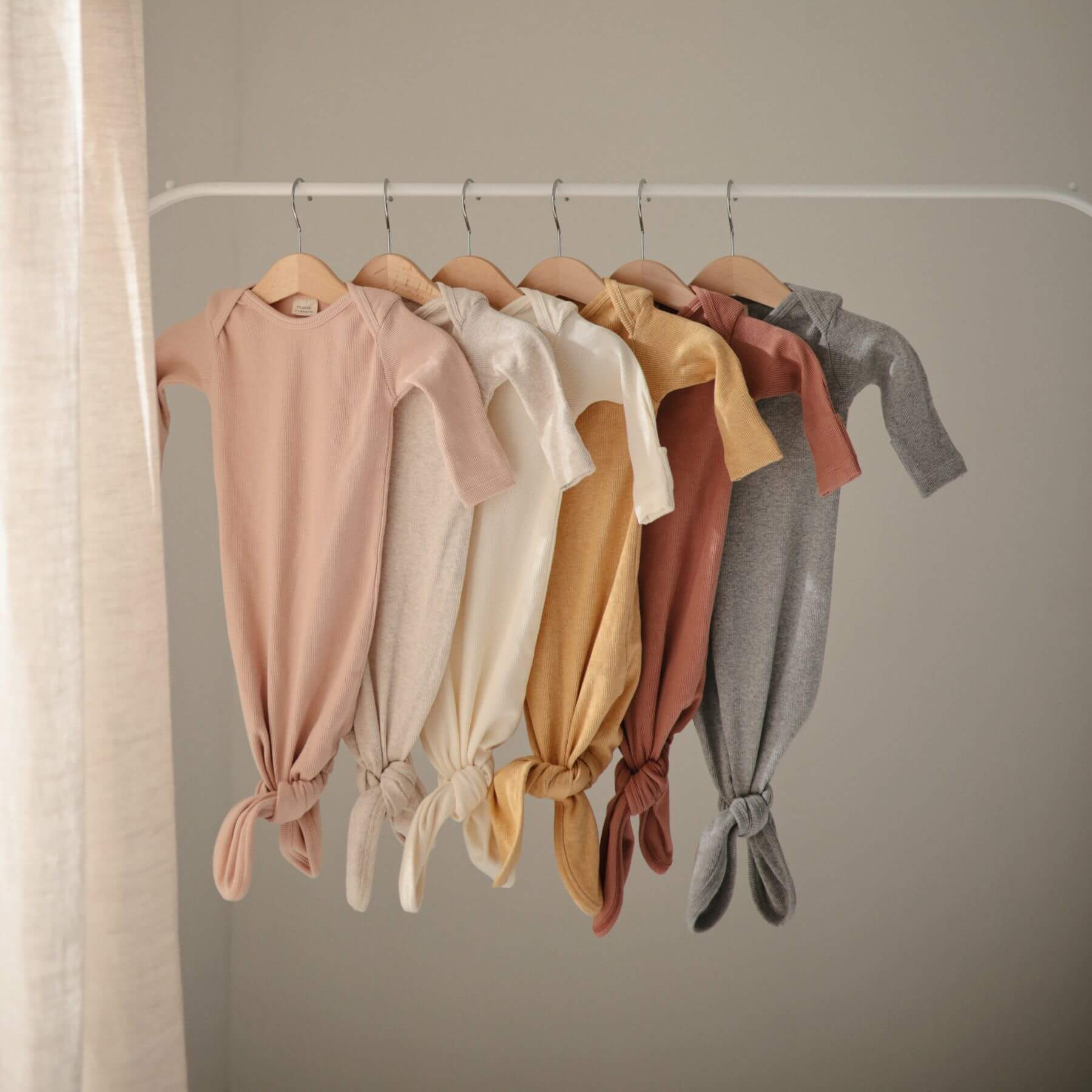 Row of baby gowns in various colors hanging on a rack against a neutral background
