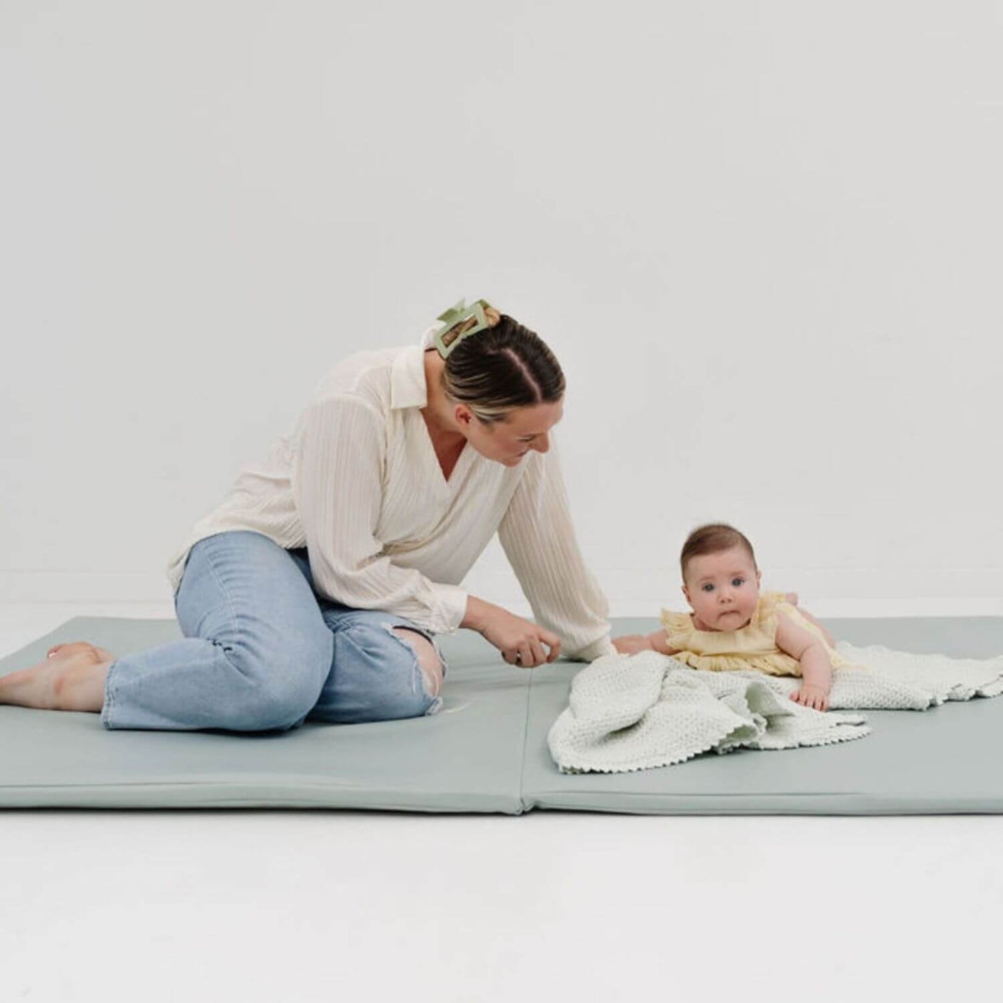 Woman and baby on a large mat with a plain background