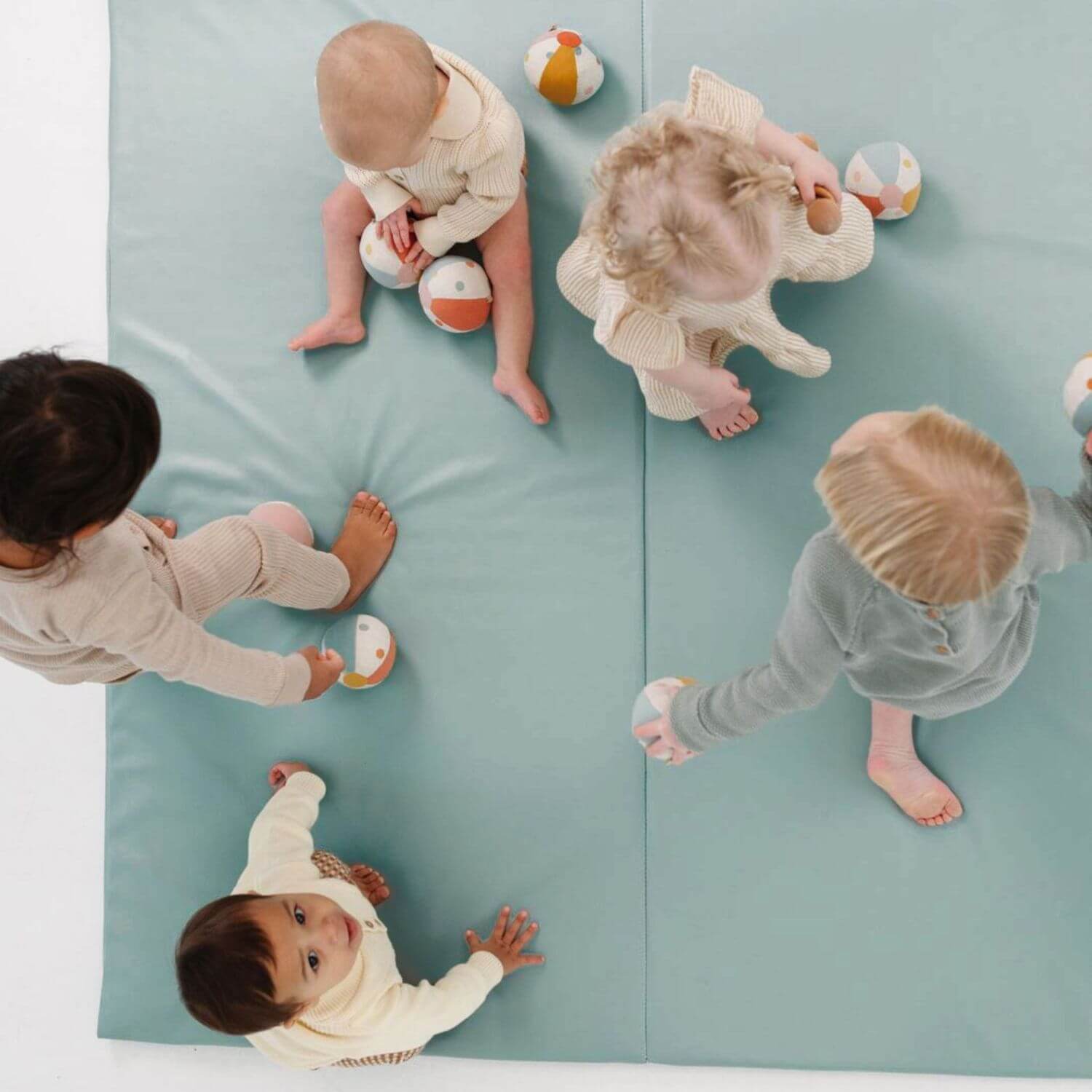 Five babies playing on Toki Kids Sage Vegan Leather Mat with colorful toys.