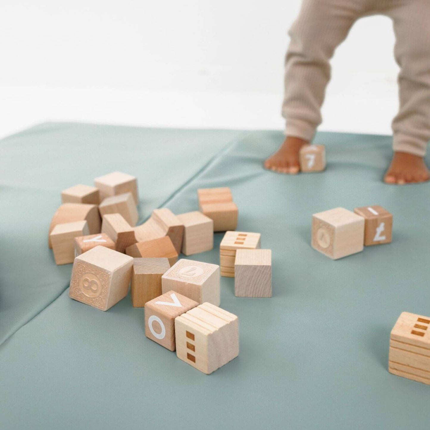 Wooden blocks with letters on Toki Kids Sage Vegan Leather Mat, child's feet visible