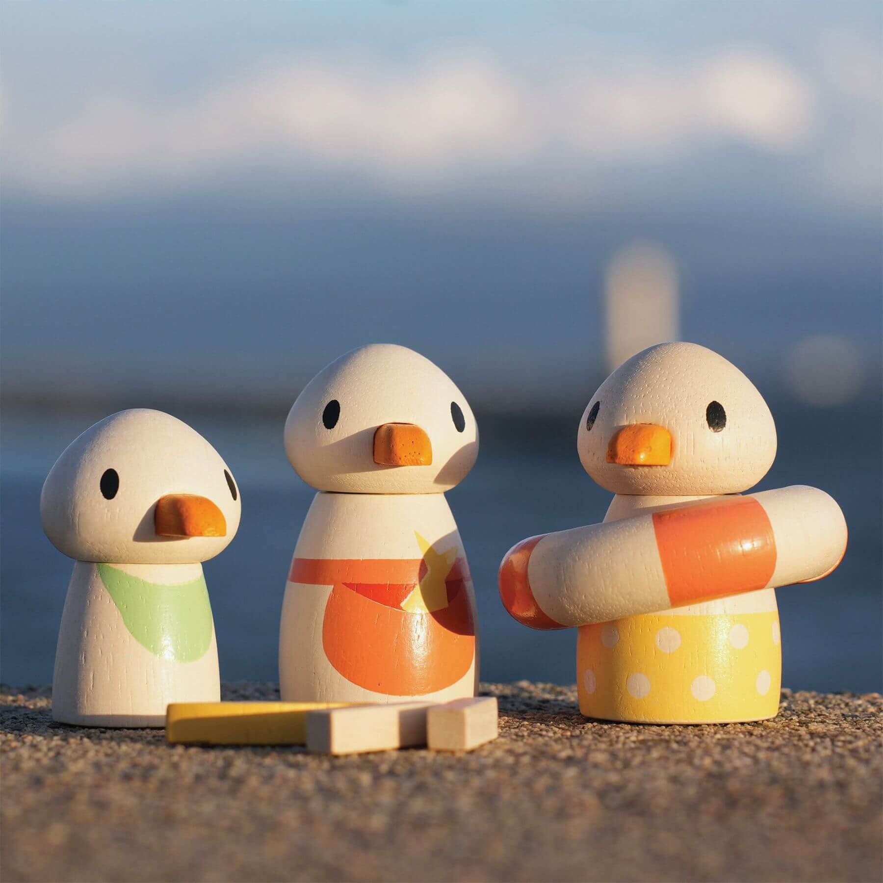 Three colorful duck-shaped toys on a sandy beach with ocean in the background