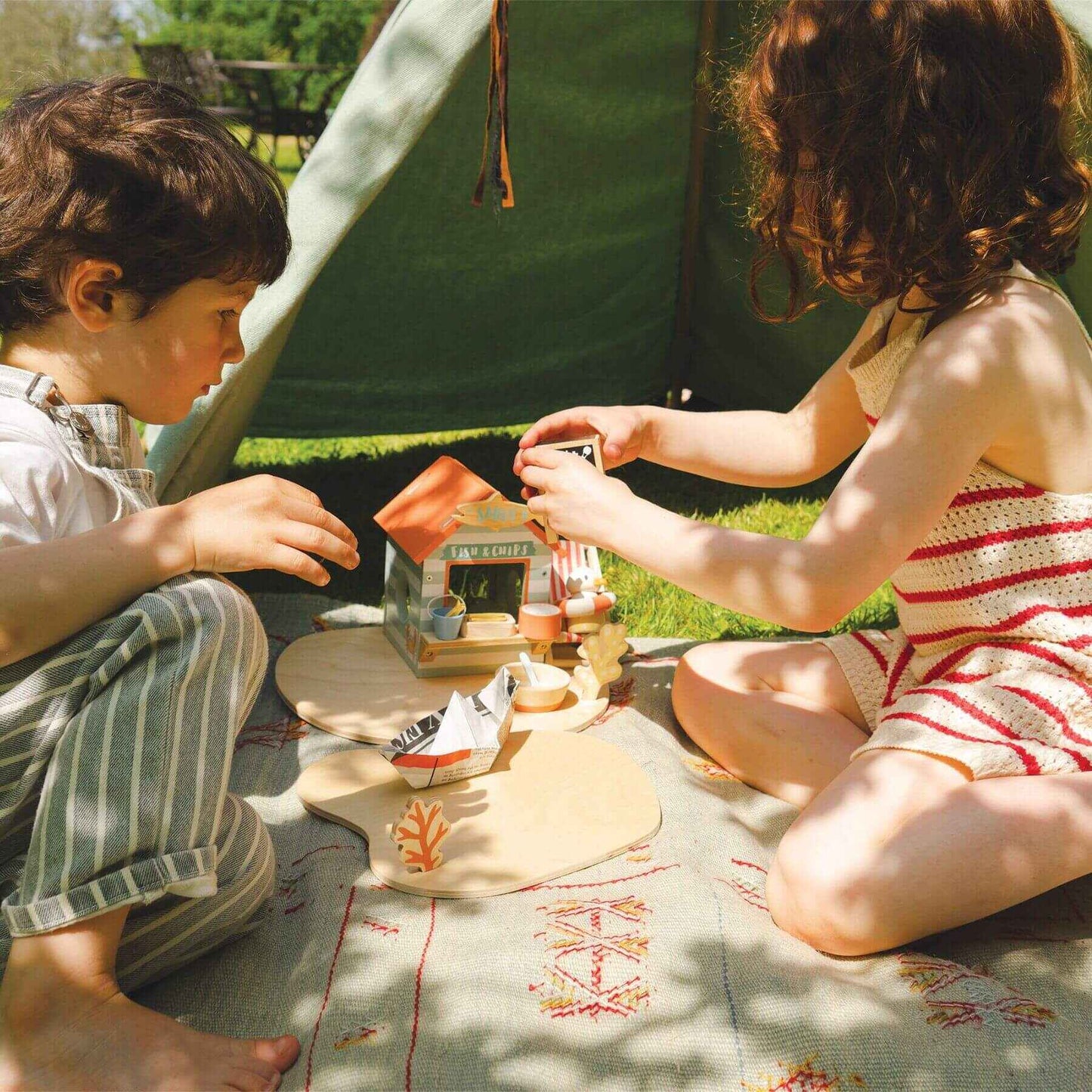 Two children playing with Tender Leaf Sandy's Beach Hut on a blanket outdoors near a tent.