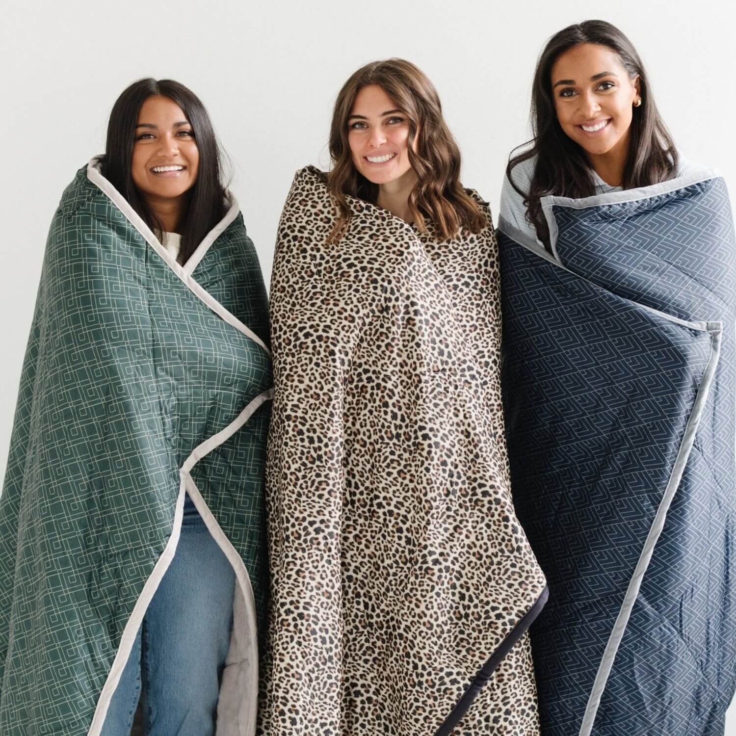 Three women wrapped in different patterned blankets against a white background