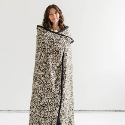 Woman wrapped in Saranoni Outdoor Blanket against a white background