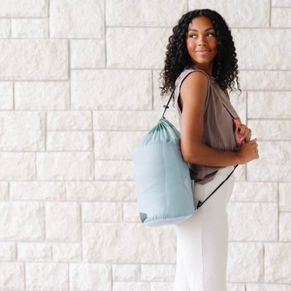 Woman holding a light blue drawstring bag against a white brick wall