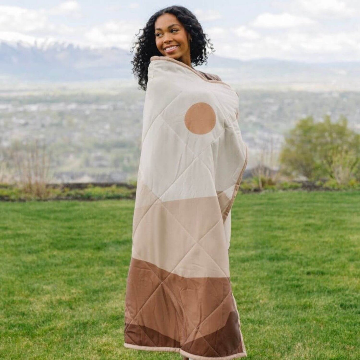 Woman wrapped in Saranoni Outdoor Blanket standing in a grassy field.