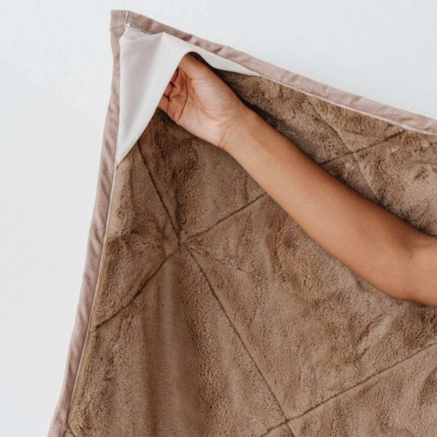 Saranoni Outdoor Blanket with a hand lifting a corner, on a light background