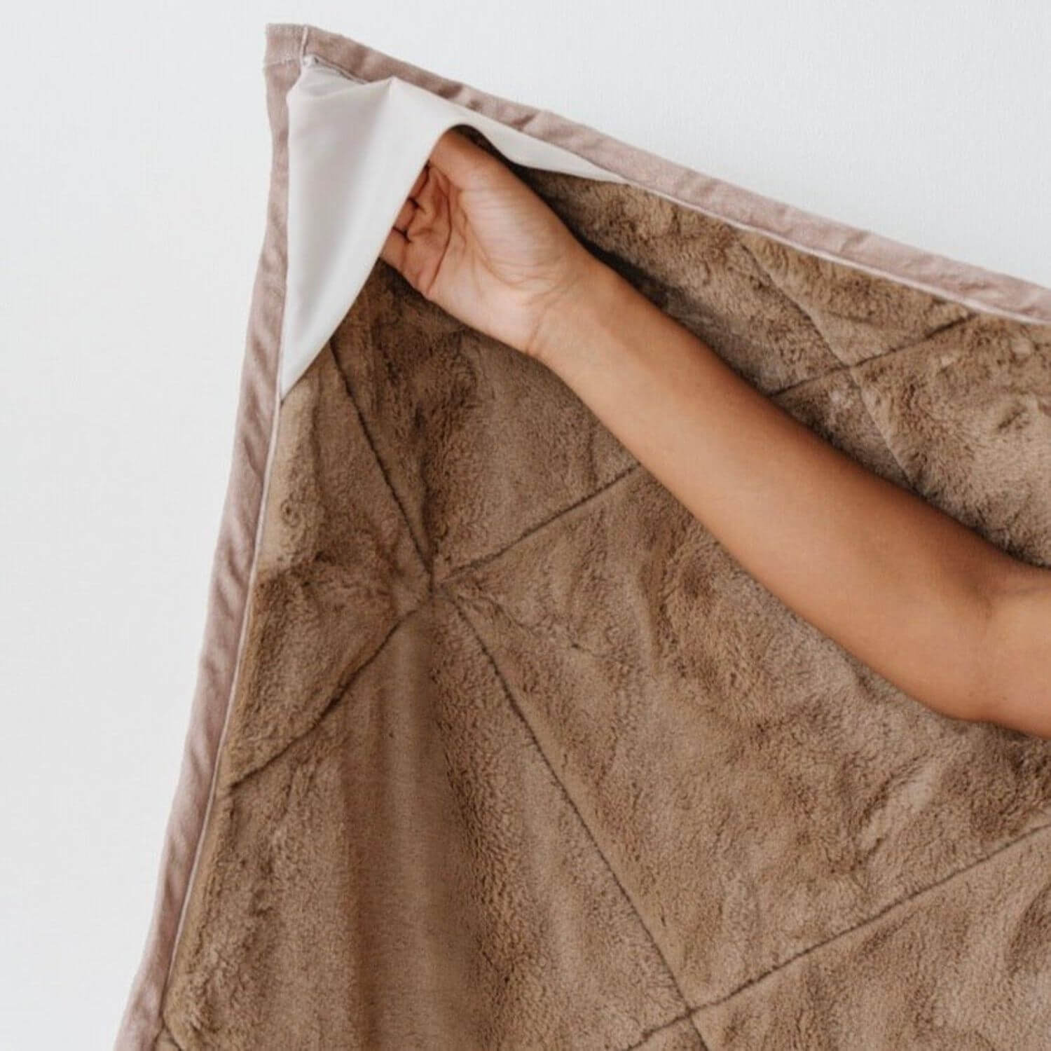 Saranoni Outdoor Blanket with a hand lifting a corner, on a light background
