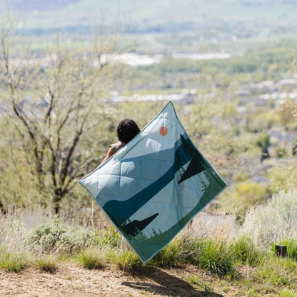 Person holding Saranoni Outdoor Blanket in a scenic outdoor setting