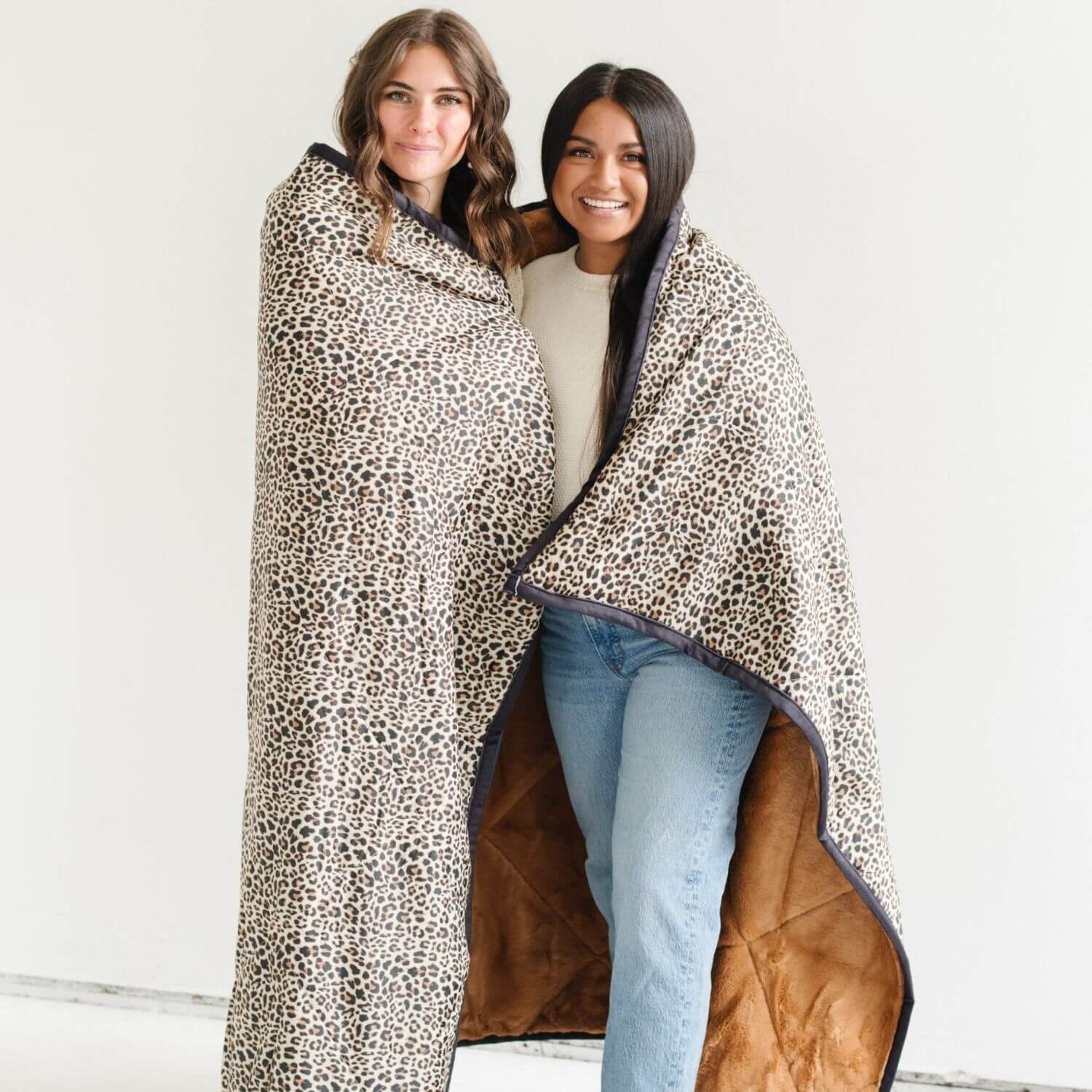 Two women wrapped in Saranoni Outdoor Blanket on a white background