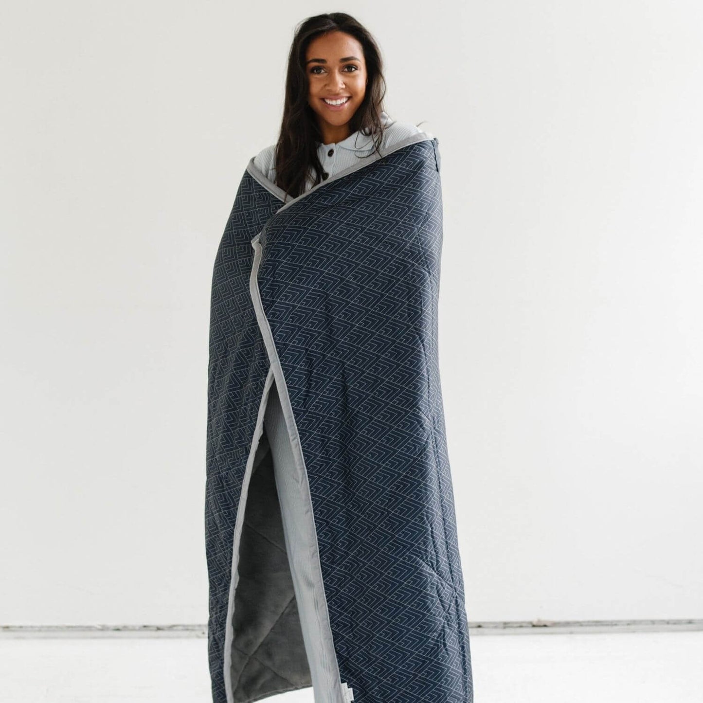 Woman wrapped in Saranoni Outdoor Blanket against a white background