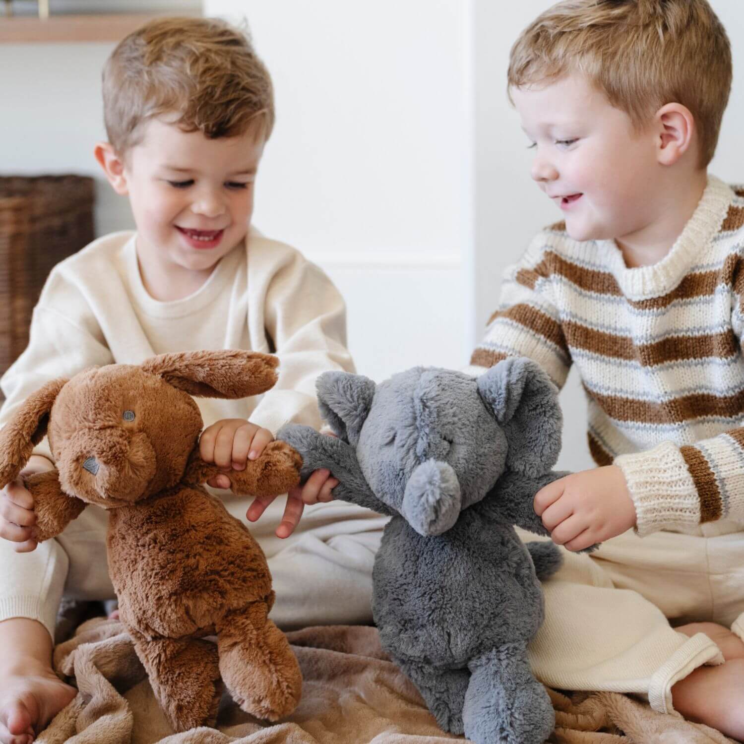 Two children playing with stuffed animals on a blanket