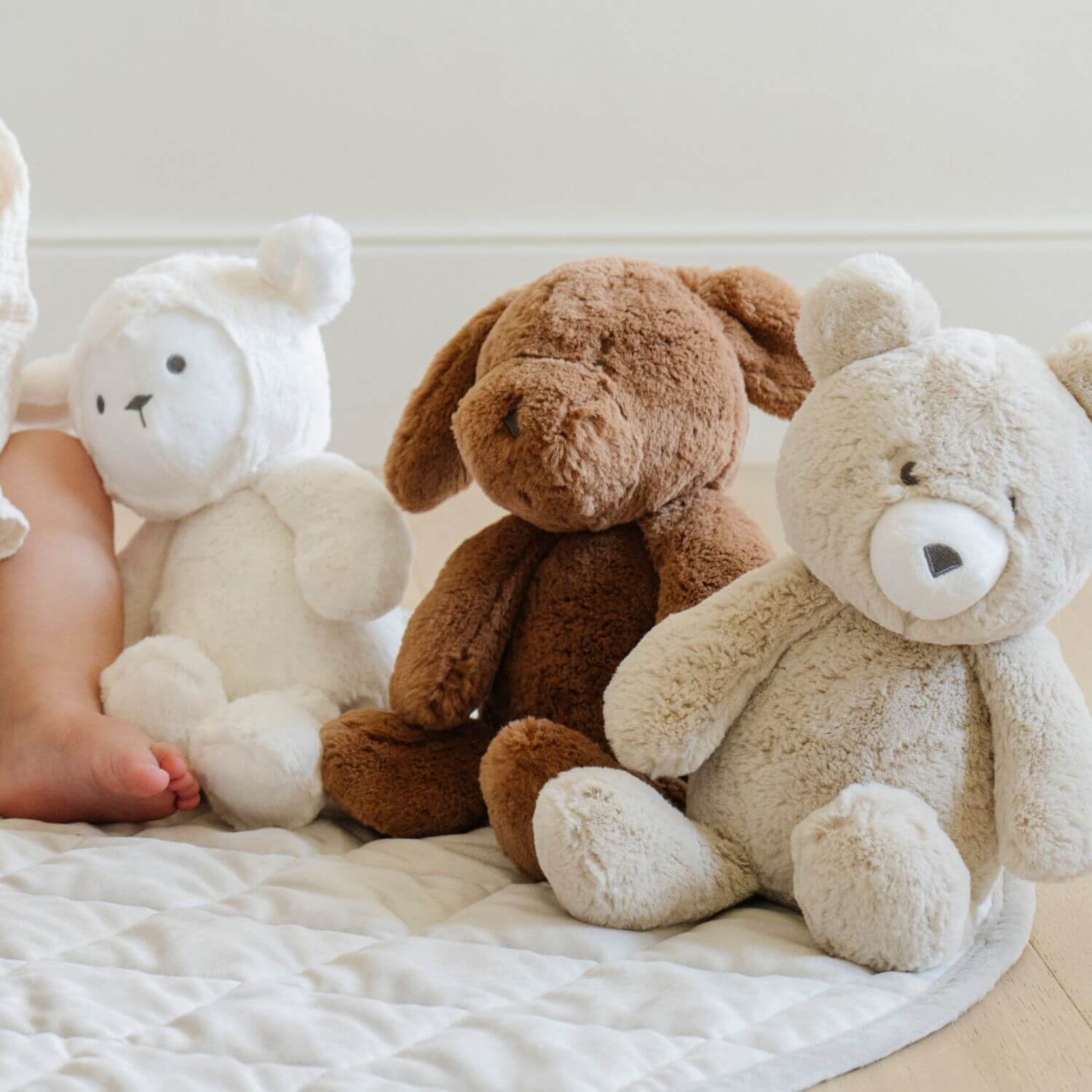 Three Saranoni Stuffed Animals sitting on a white surface with a child's feet visible.