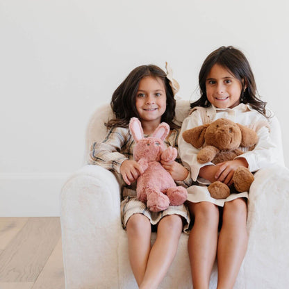 Two young girls sitting on a white chair holding stuffed animals.