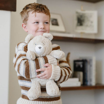 Child holding Saranoni Stuffed Animal bear in a striped sweater indoors