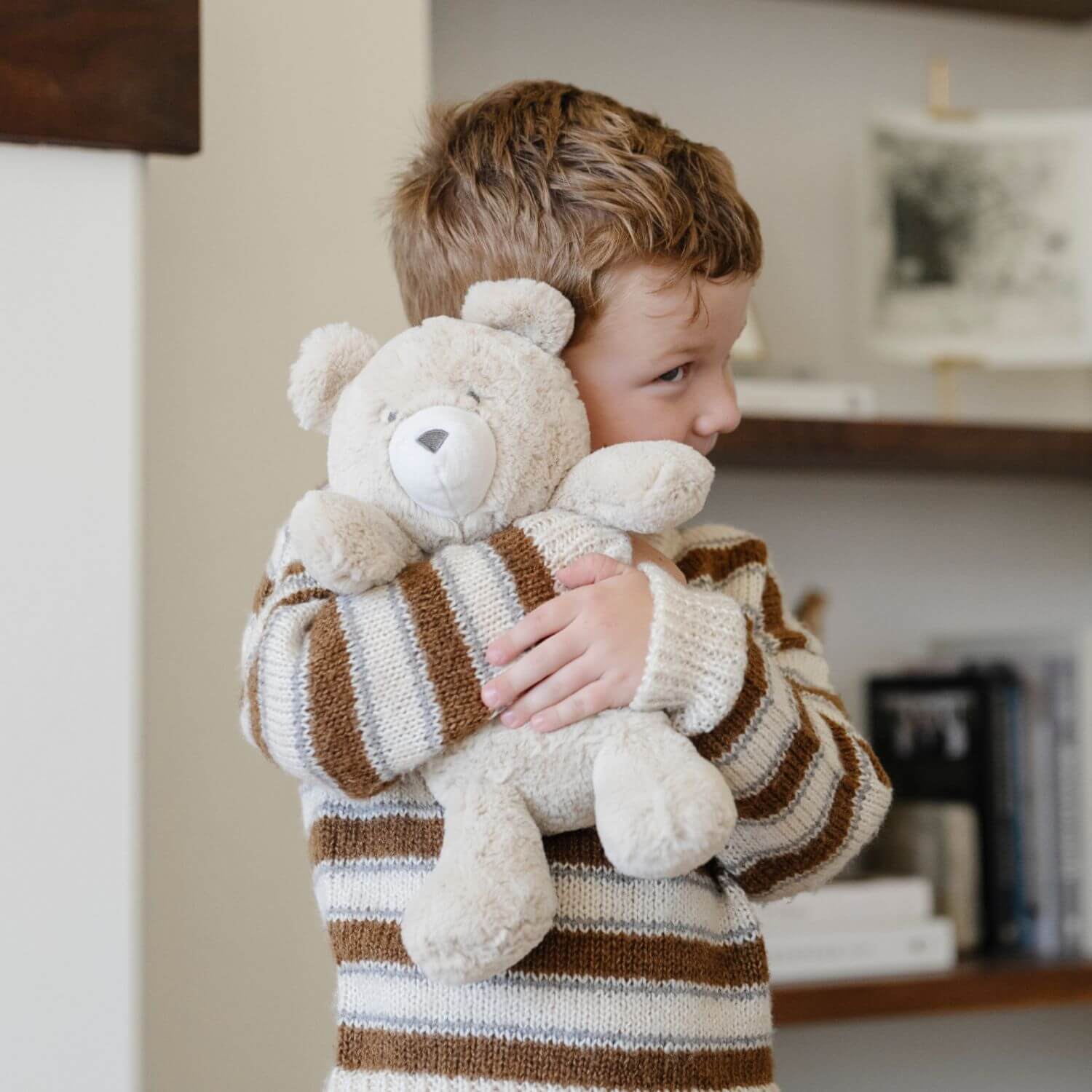 Child holding Saranoni Stuffed Animal bear in a striped sweater indoors