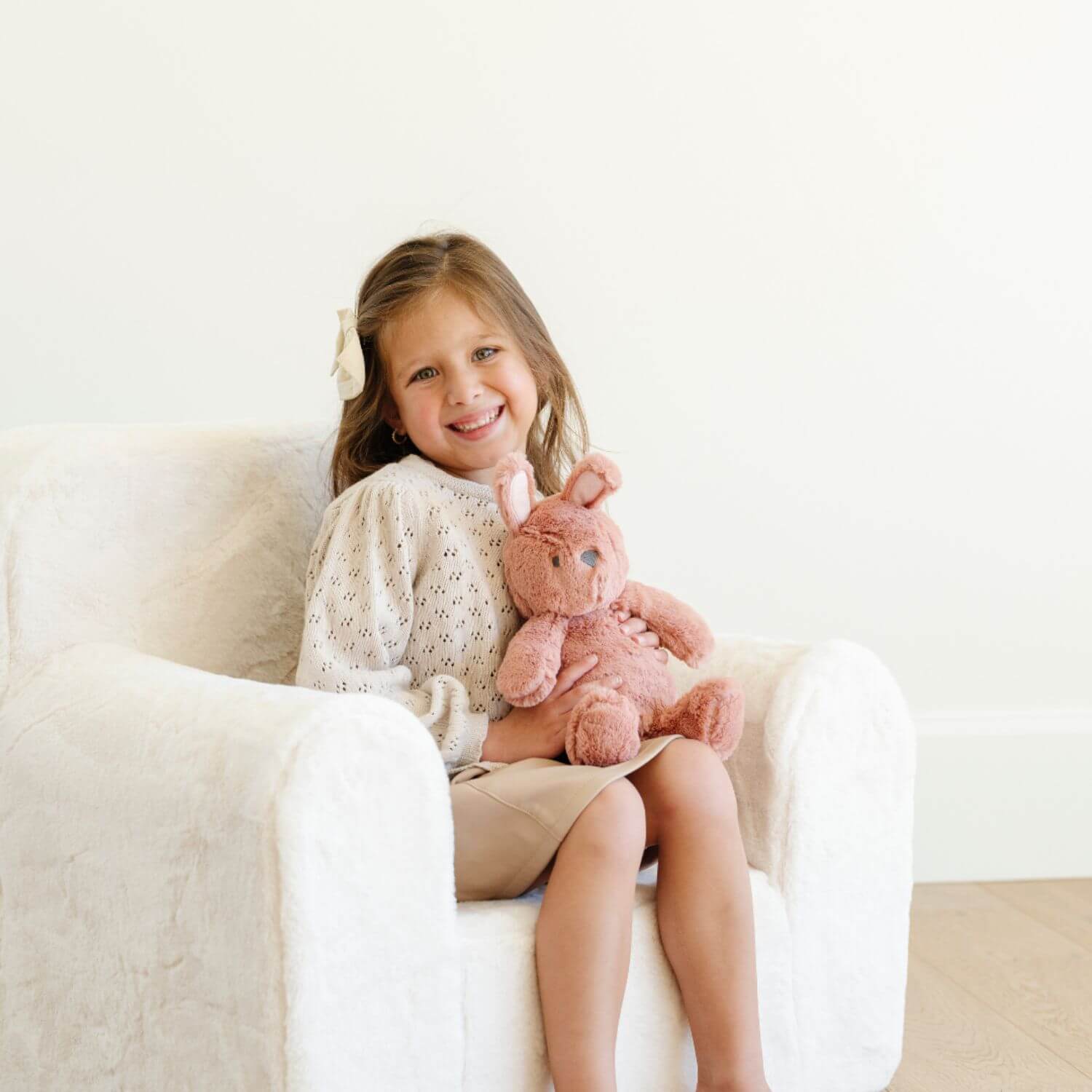 Young girl sitting on a white couch holding Saranoni Stuffed Animal bunny