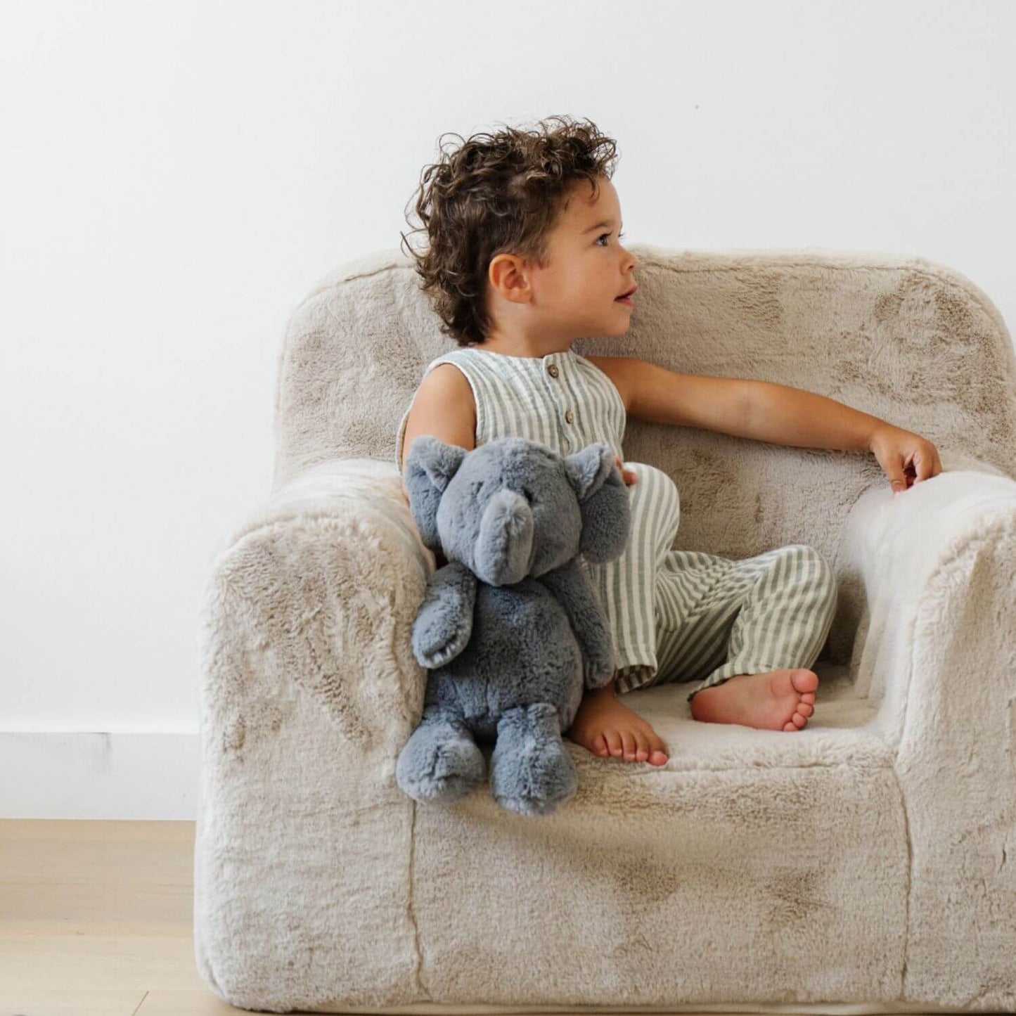 Child sitting on a plush chair holding Saranoni Stuffed Animal elephant in a bright room.