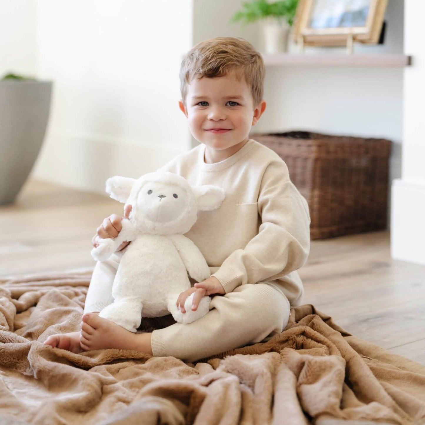 Child sitting on a bed holding Saranoni Stuffed Animal lamb in a cozy room.