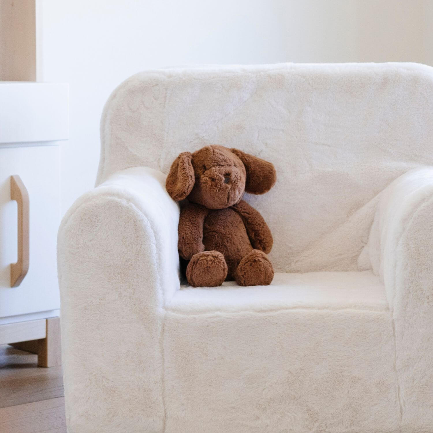 Brown Saranoni Stuffed Animal Puppy sitting on a white armchair in a minimalistic room.