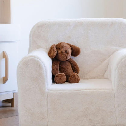 Brown Saranoni Stuffed Animal Puppy sitting on a white armchair in a minimalistic room.