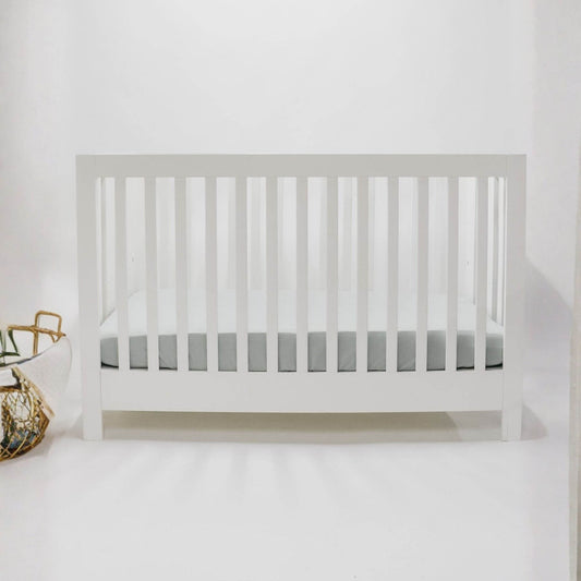 White crib with Little Mae & Co Seafoam Ribbed Crib Sheet against a white wall