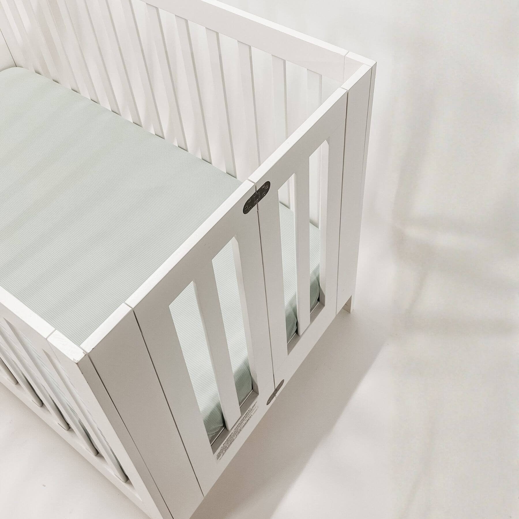 White crib with a mattress covered with Little Mae & Co Seafoam Ribbed Crib Sheet