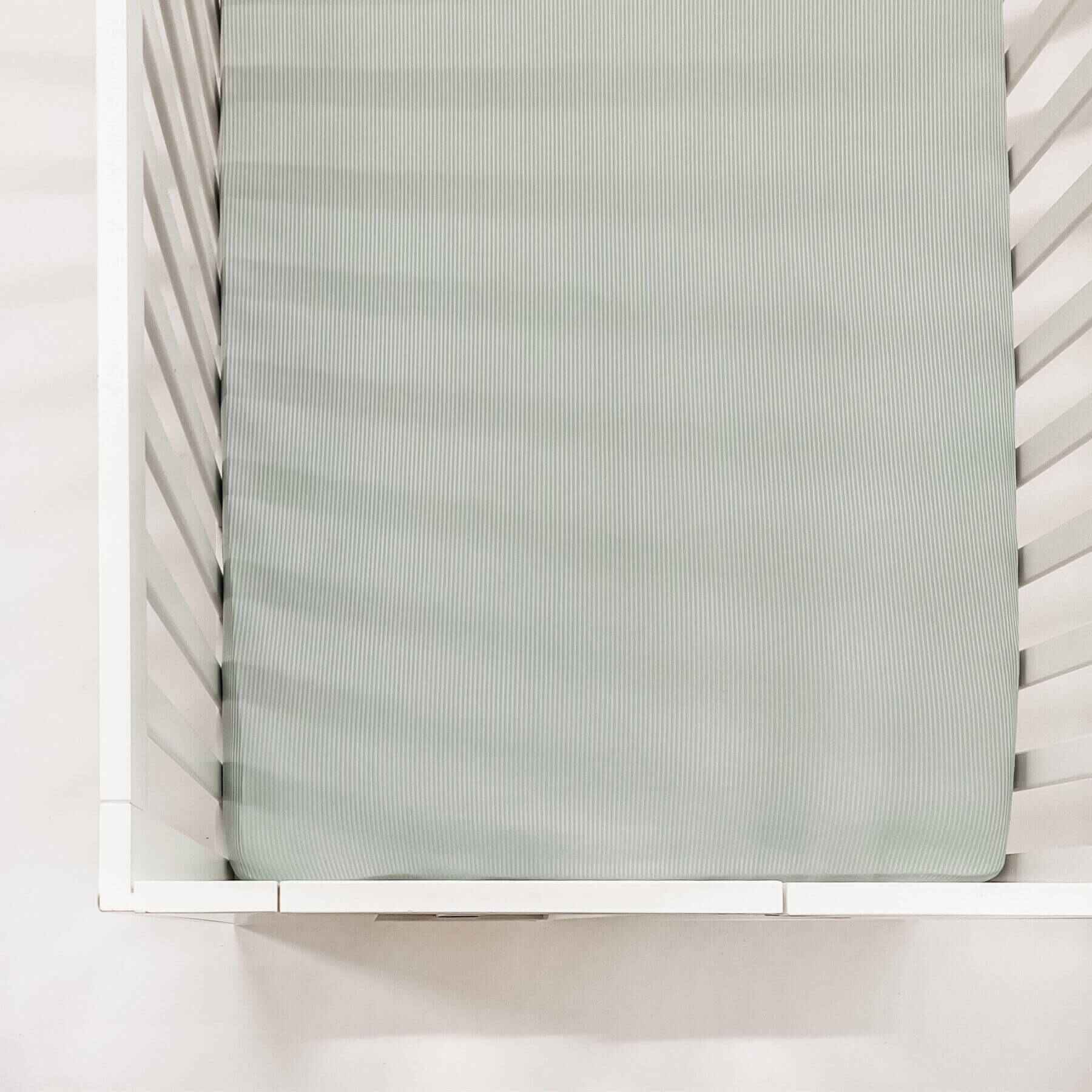 White crib with a mattress covered with Little Mae & Co Seafoam Ribbed Crib Sheet