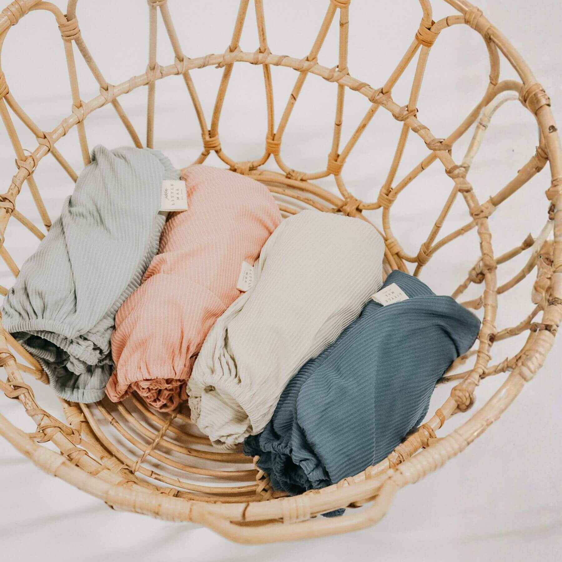 Folded Little Mae & Co Seafoam Ribbed Crib Sheets in a wicker basket on a light background