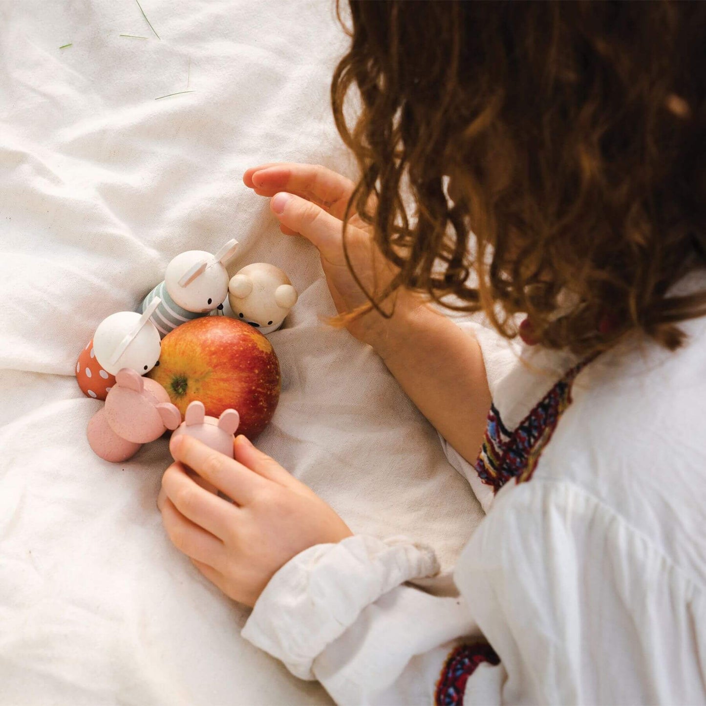 Child playing with toys and an apple on a white blanket