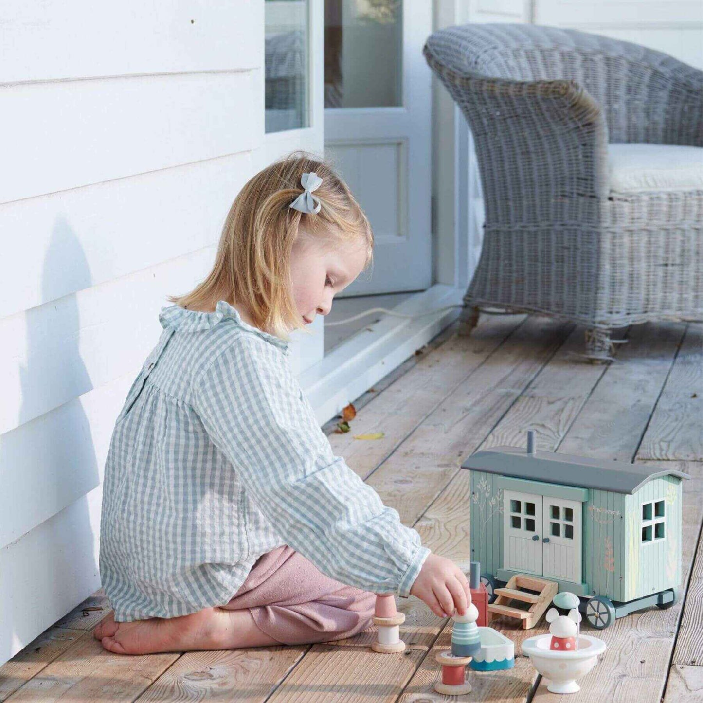 Young girl playing with Tender Leaf Secret Meadow Shepherd’s Hut on a wooden deck.