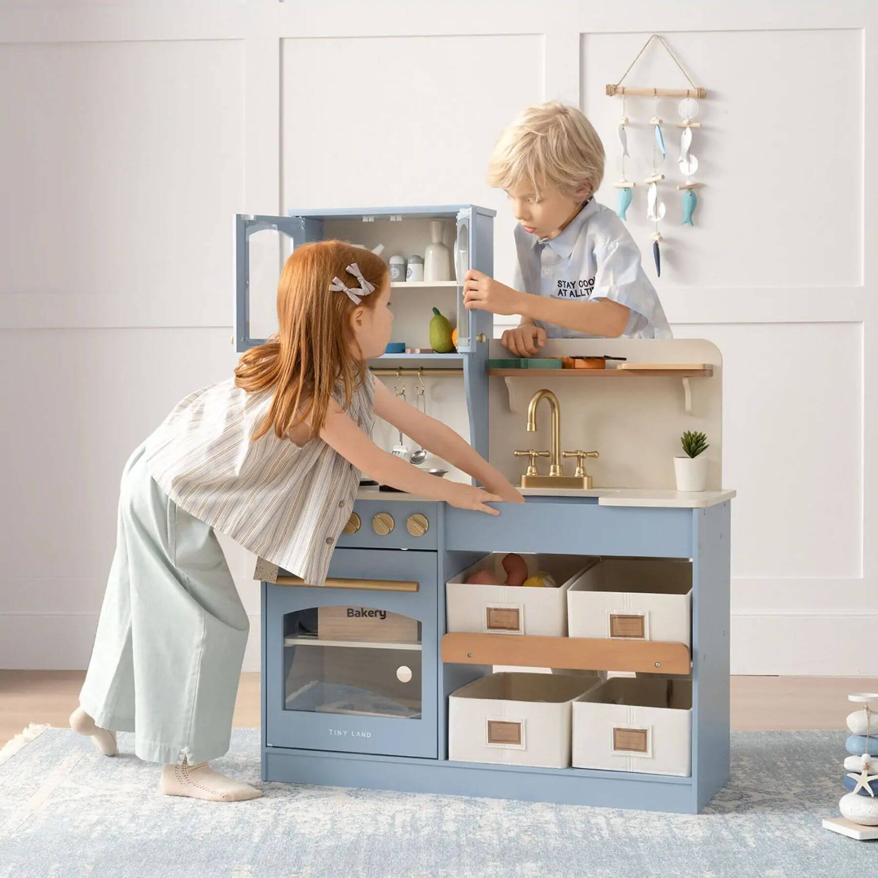 Two children playing with Tiny Land® Serenity Play Kitchen Lagoon Blue in a room with a white wall.