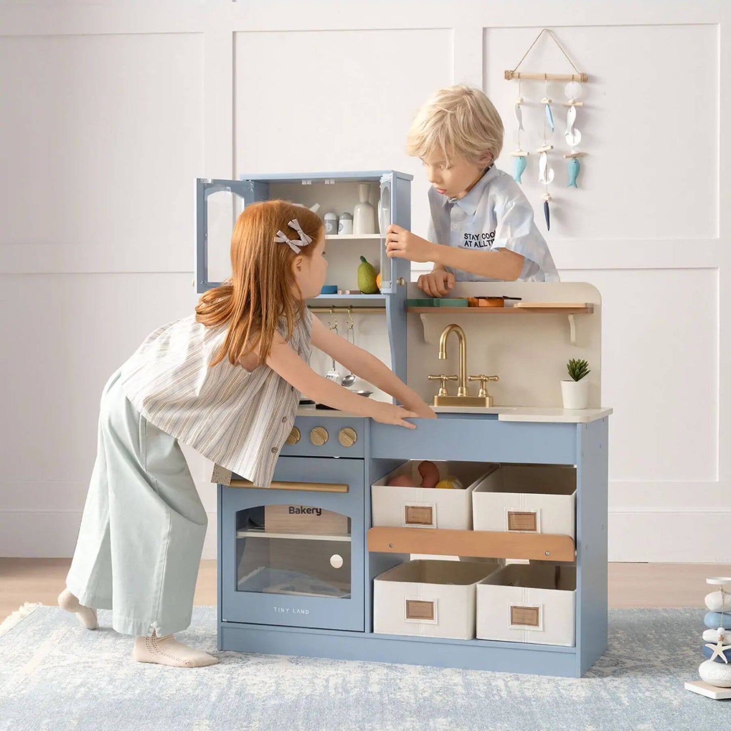 Two children playing with Tiny Land® Serenity Play Kitchen Lagoon Blue in a room with a white wall.