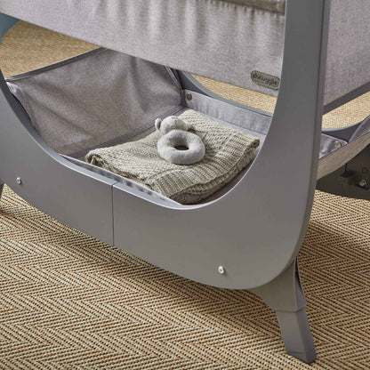Gray baby crib with a blanket and toy on a textured floor