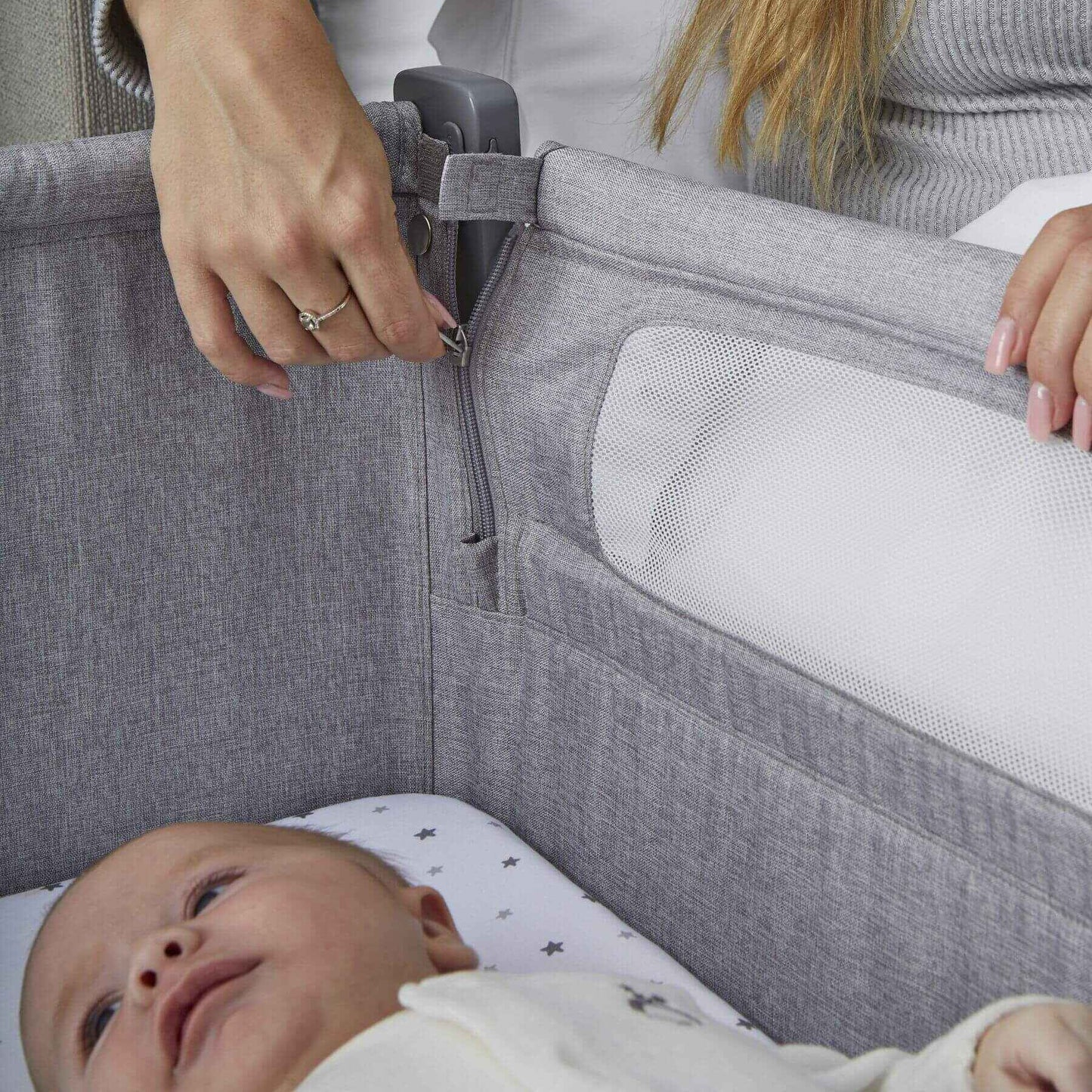 Baby lying in a gray crib with a person adjusting the side rail.