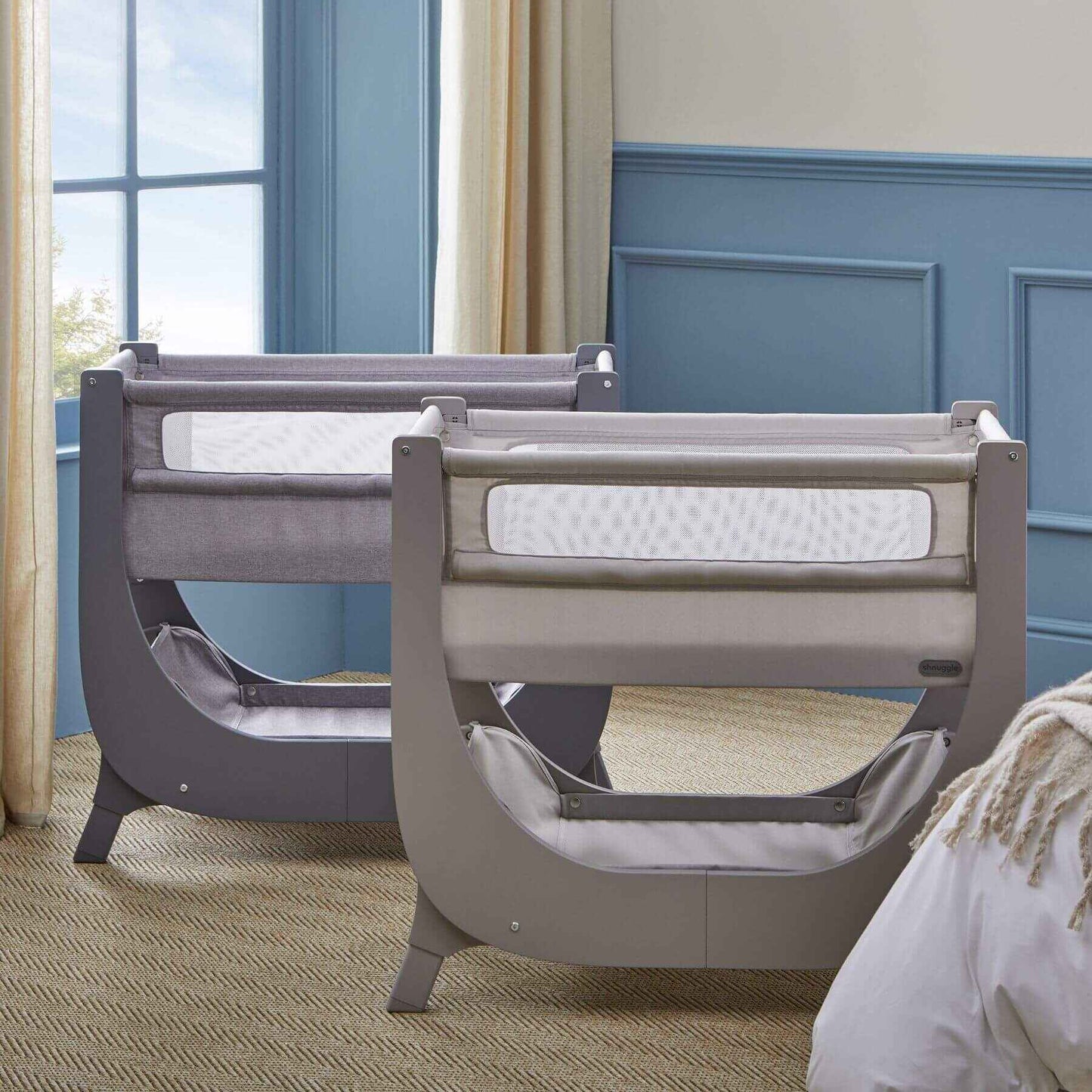 Two Shnuggle Air Lite Bedside Bassinets in a room with blue walls and a window.