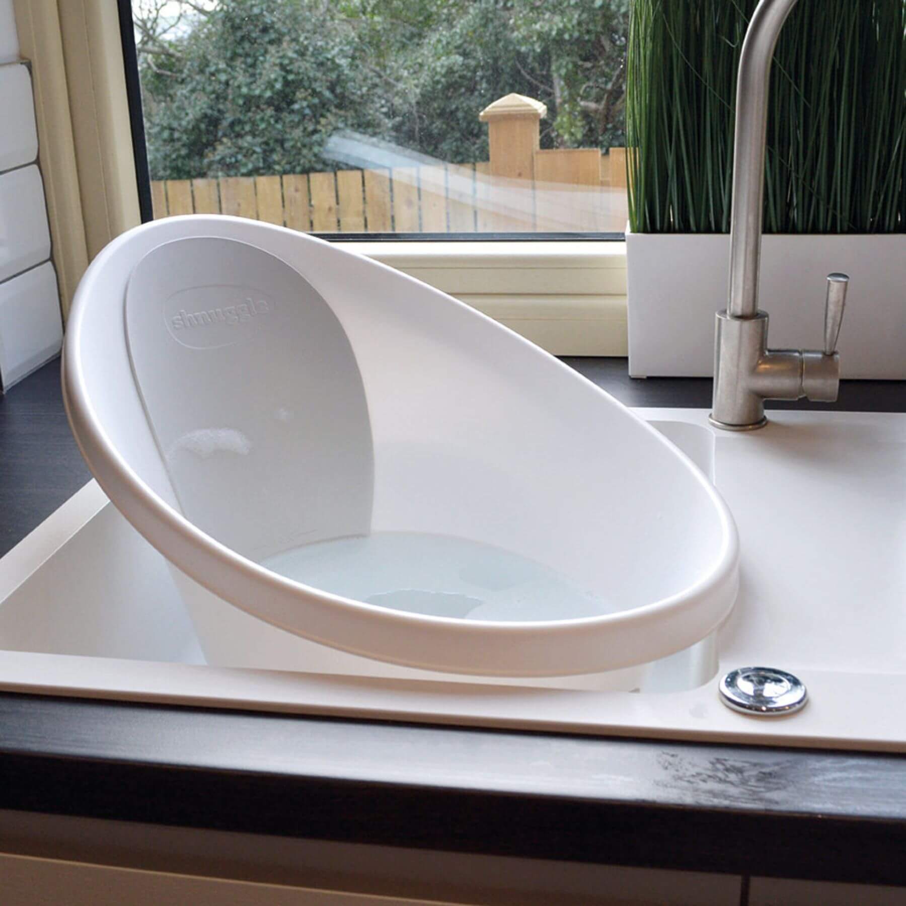 Shnuggle Bath seat in a sink with a window and plant in the background