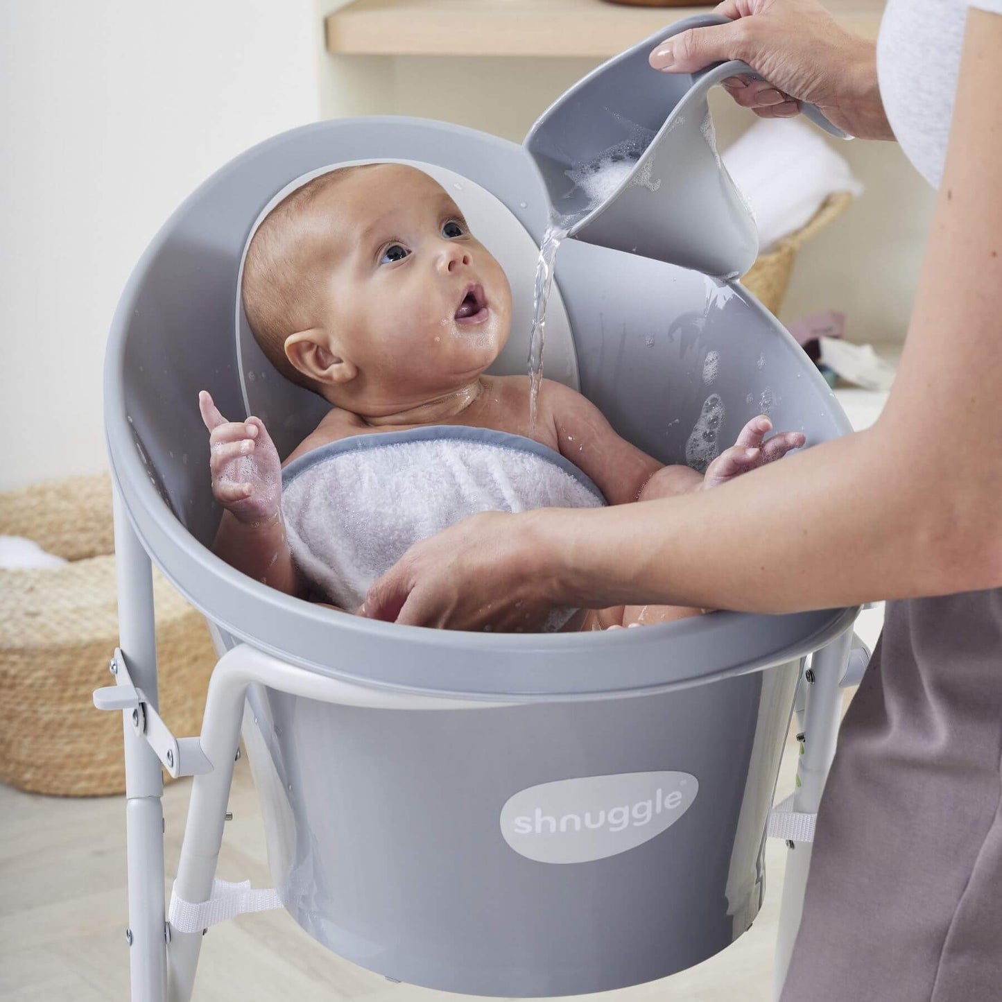 Baby being bathed in a Shnuggle baby bath seat with water being poured over them.